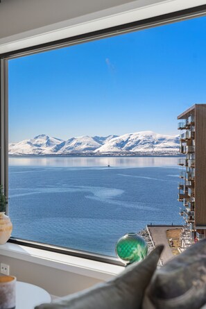 Ein Zimmer mit großem Fenster mit Blick auf ein Gewässer und schneebedeckte Berge.