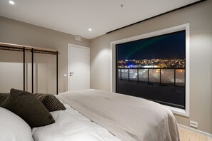 A bedroom with a large window, a bed, a wardrobe, and a view of a cityscape at night. - Eight floor Premium Penthouse with Scenic View (Tromsø)