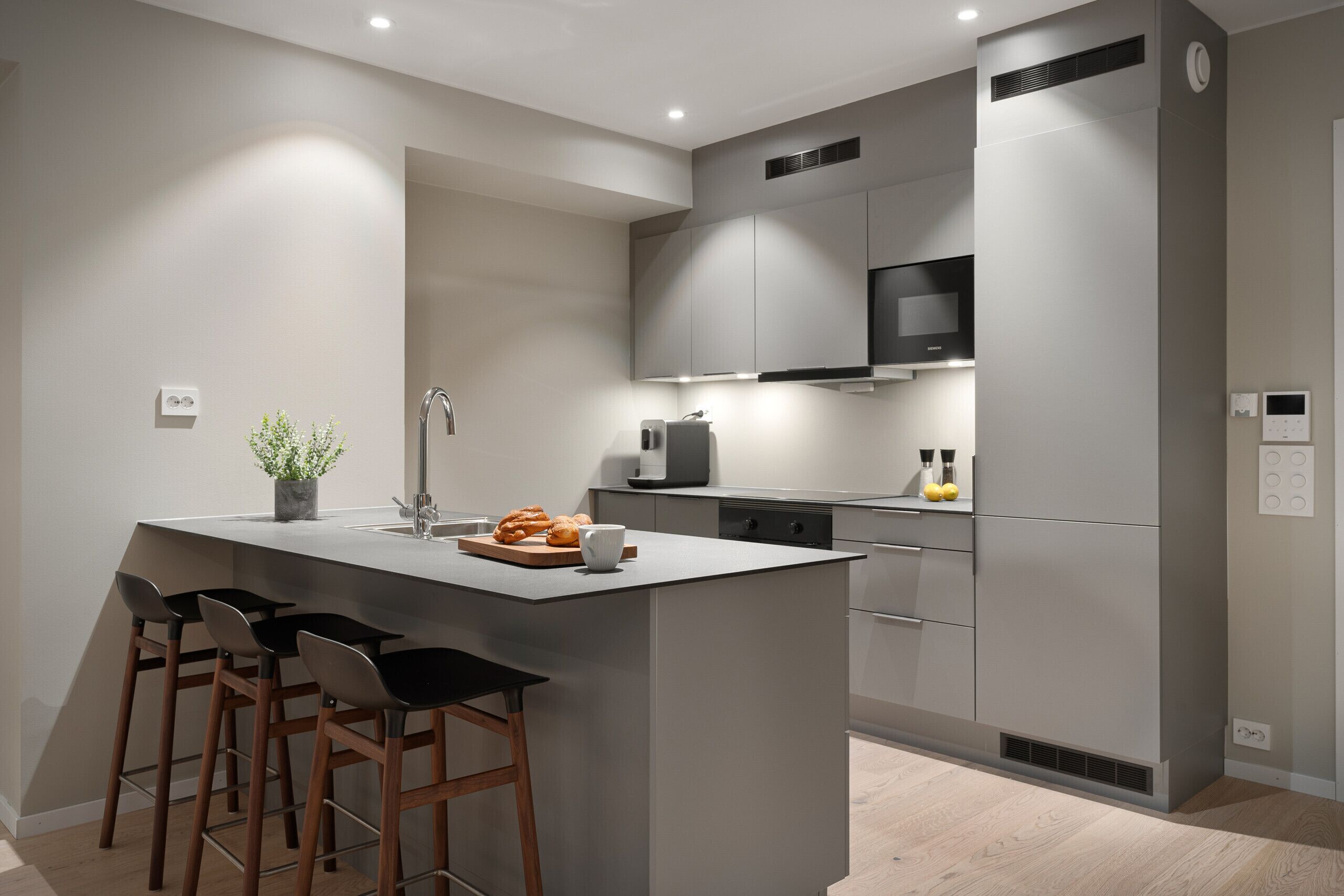 A modern kitchen with a central island, bar stools, a built-in oven, and a microwave.