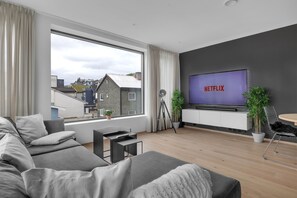 Ein modernes Wohnzimmer mit großem Fenster, grauem Sofa, Flachbildfernseher und Stativ.