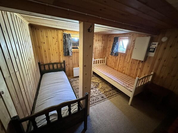 Une cabine avec deux lits en bois, une petite fenêtre et un placard blanc.