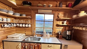 A compact kitchen with wooden walls, a window with a view, and various kitchenware. - Lofoten Horizon, Fredvang (Flakstad)