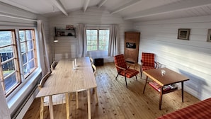 A room with a wooden table, two chairs, a cabinet, and a window with curtains. - Lofoten Horizon, Fredvang (Flakstad)