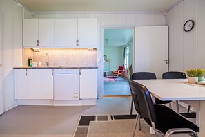 A compact kitchen with white cabinets, a built-in dishwasher, and a dining area with a table and chairs.