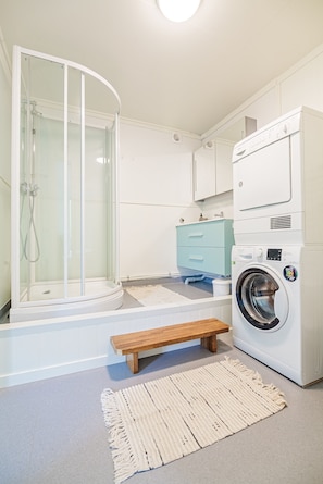 Une buanderie équipée d’un lave-linge, d’un banc et d’une douche fermée par des parois en verre.