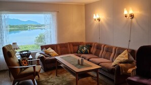 A living room with a sofa, armchairs, a coffee table, and a view of a lake and mountains through a window.