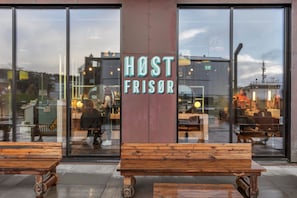 Ein Gebäude mit einem 'HOST FRISOR' Schild, Holzbanken vor der Fassade und großen Fenstern, die das Innere reflektieren.