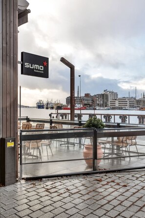 Ein Restaurant am Wasser mit Terrassensitzgelegenheiten, einem Schild mit der Aufschrift 'SUMO Restaurant' und Blick auf das Wasser sowie die Stadtlandschaft.