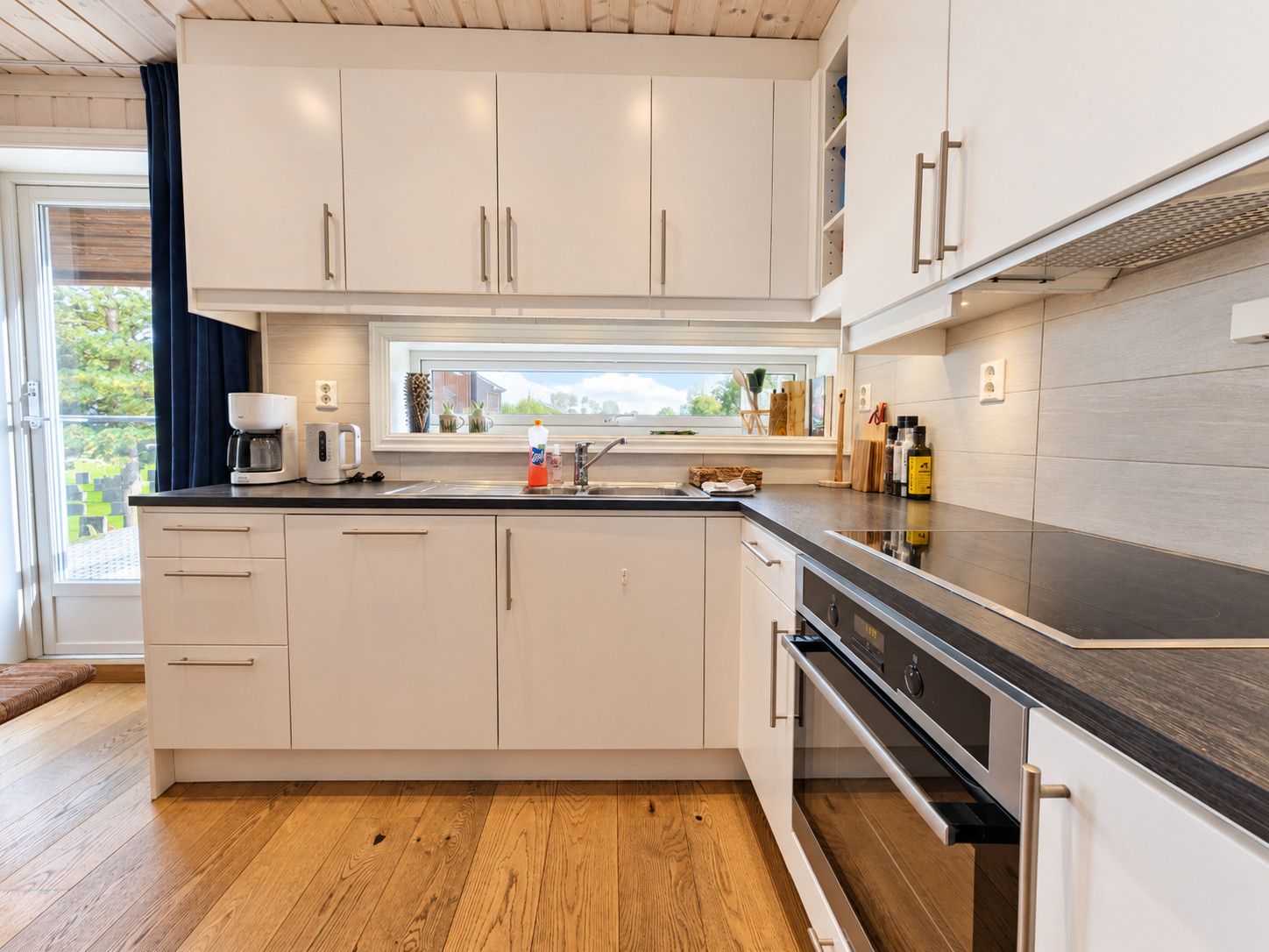 Una cocina moderna con muebles blancos, encimera negra y ventana con vistas a follaje.