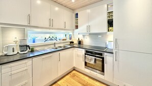 Una cocina moderna con armarios blancos, un horno de acero inoxidable y un ventanal con vistas a árboles.