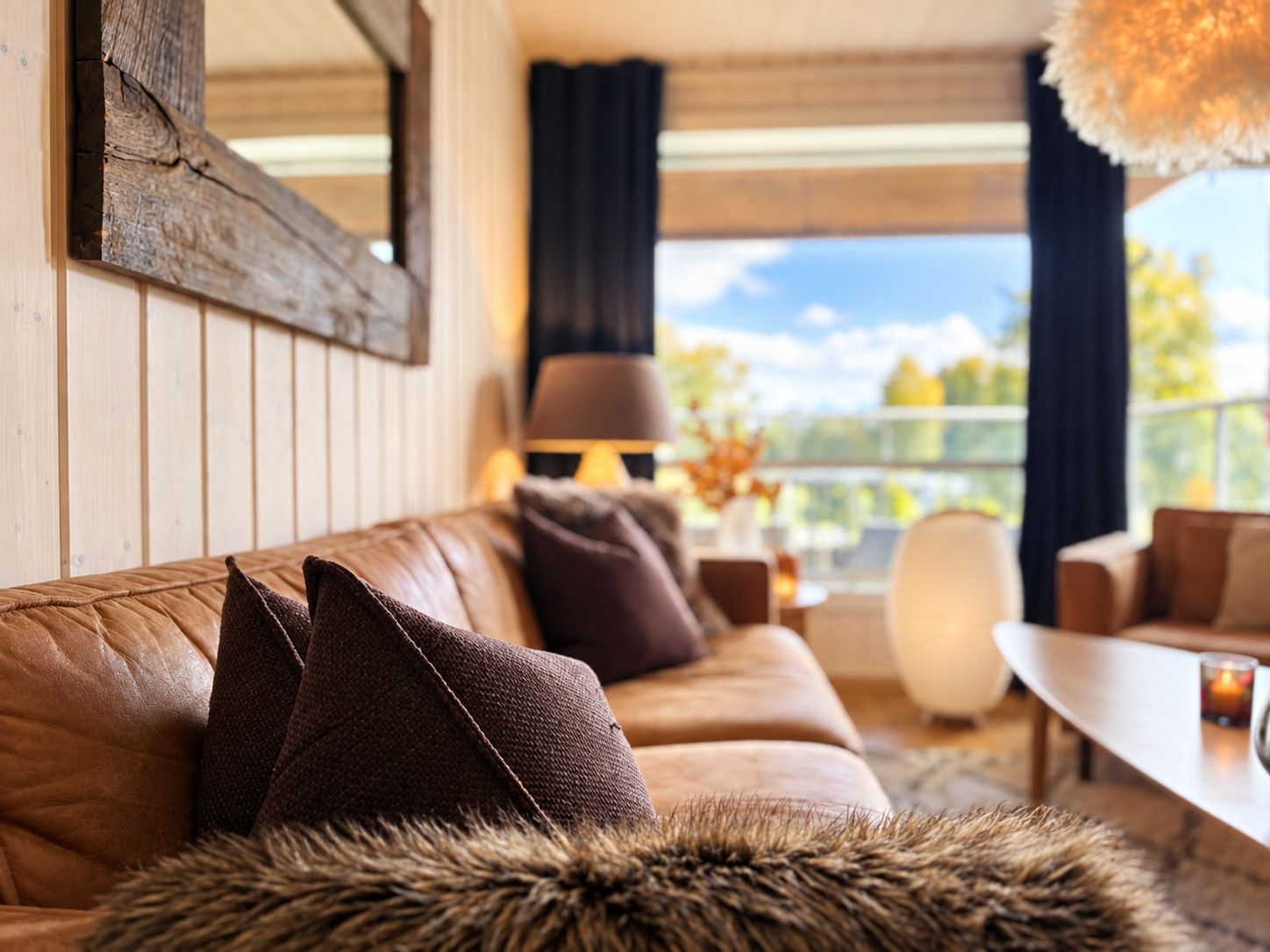 A cozy living room with a leather sofa, fur throw, and a view of the outdoors.