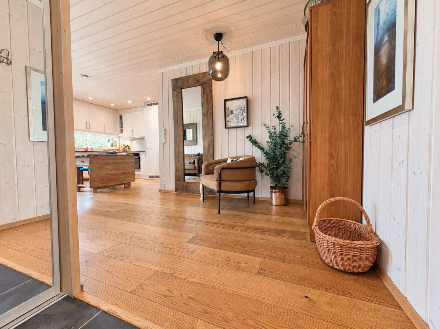 Quarto amplo com piso de madeira, sofá de couro marrom, planta em vaso e cesta de vime.