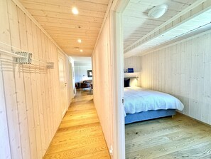Een smalle gang met houten wanden en vloeren, die leidt naar een slaapkamer met een bed en nachtkastje.