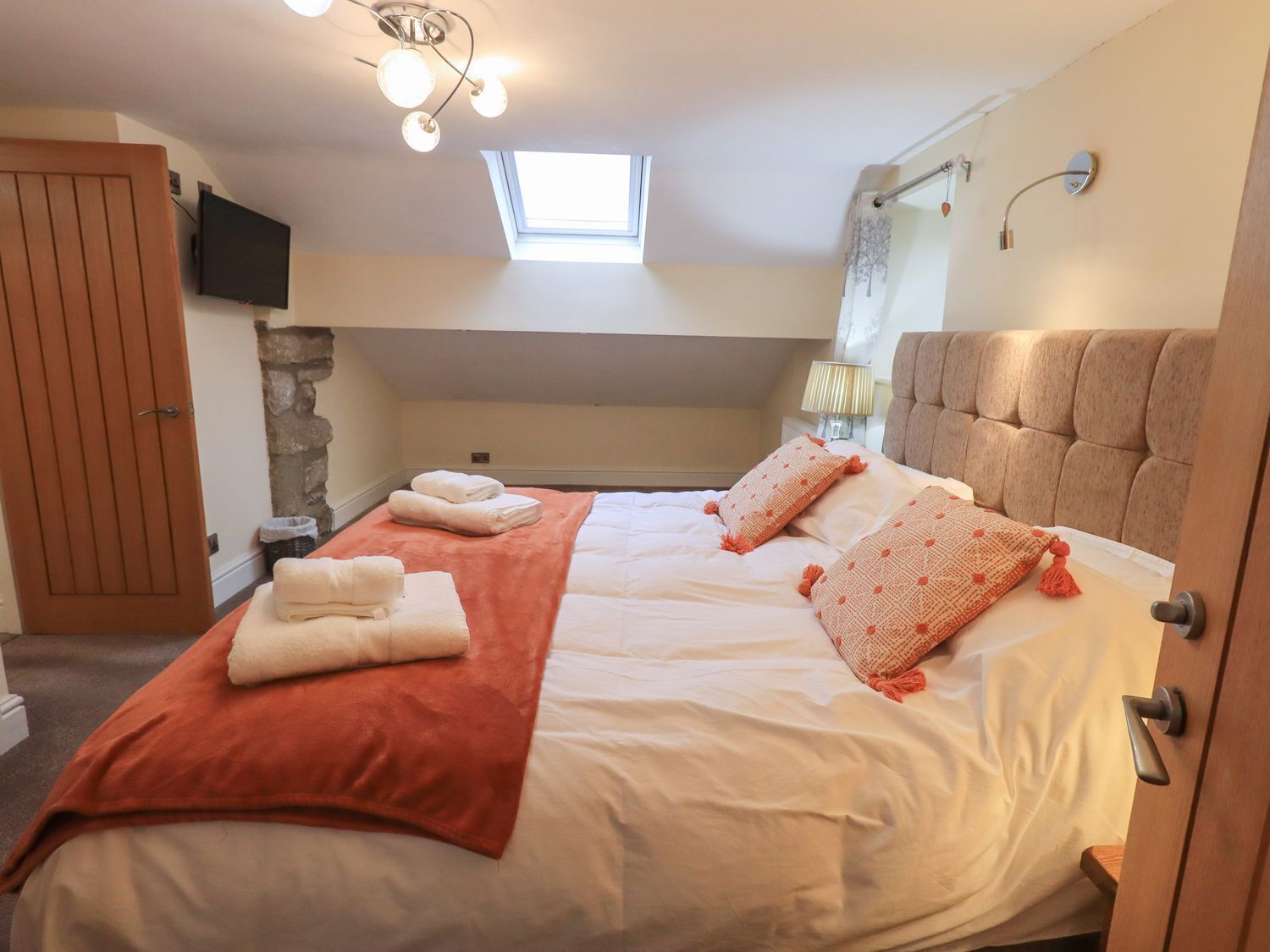 A bedroom with a bed, a TV, a window, a shower, and a door.