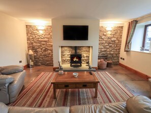 Ein Wohnzimmer mit Kamin aus Stein, einem Wand-Fernseher, Ledersofas und einem Couchtisch aus Holz.