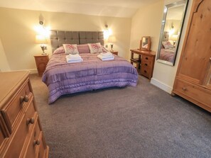 A bedroom with a bed, two bedside tables, a dresser, a mirror, and a carpeted floor. - Orcaber Farm Barn (Lancaster)