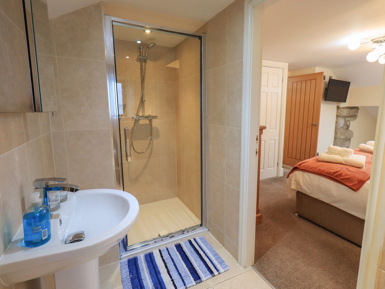 A bathroom with a glass-enclosed shower, a white sink, and a blue towel on the floor.