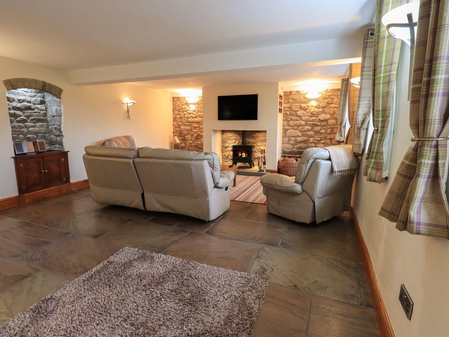 A living room with a stone fireplace, leather sofas, and a flat-screen TV.