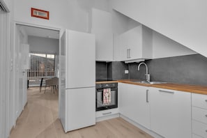 Una cucina moderna con mobili bianchi, un piano di lavoro in legno, un forno integrato e una zona pranzo visibile con tavolo e sedie.