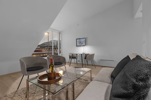 Een moderne woonkamer met een glazen salontafel, een bank met donkere kussens en een eethoek met stoelen en een tafel.