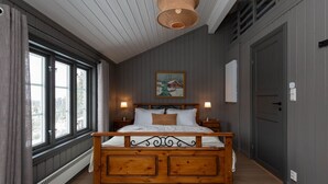 A bedroom with a wooden bed, large windows, a painting on the wall, and a ceiling light fixture.