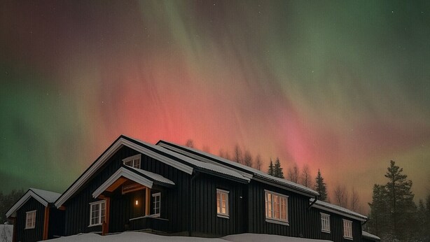 A house with a dark exterior, multiple windows, and a snow-covered landscape.