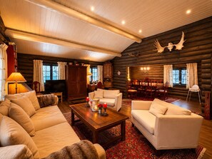 A log cabin interior with a sofa, chairs, a dining table, and a fireplace.