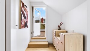 Un pasillo estrecho con una escalera de madera que lleva a una puerta abierta, un aparador de madera y un cuadro en la pared.