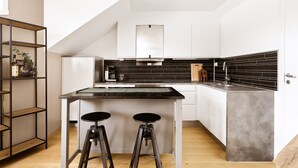 Una cocina moderna con una isla central, taburetes de bar, una estantería metálica y un salpicadero negro.