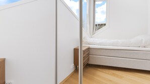 Un dormitorio con un espejo grande, una cama y una ventana que ofrece vista al cielo y a las nubes.