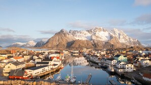 A coastal town with a harbor, boats, and a mountain range in the background.