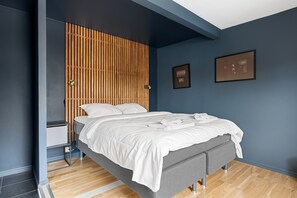A modern bedroom with a bed, wooden slat headboard, bedside tables, and framed pictures on the wall. - Trivelig leilighet i rolige, bynære omgivelser (Tromsø)