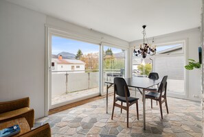 A dining area with a table and chairs, large windows, and a stone floor. - Trivelig leilighet i rolige, bynære omgivelser (Tromsø)