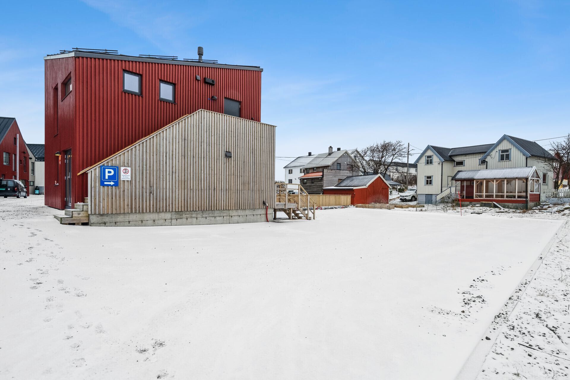 Un bâtiment rouge avec une grande porte de garage, un panneau indiquant un espace de stationnement et un sol recouvert de neige.