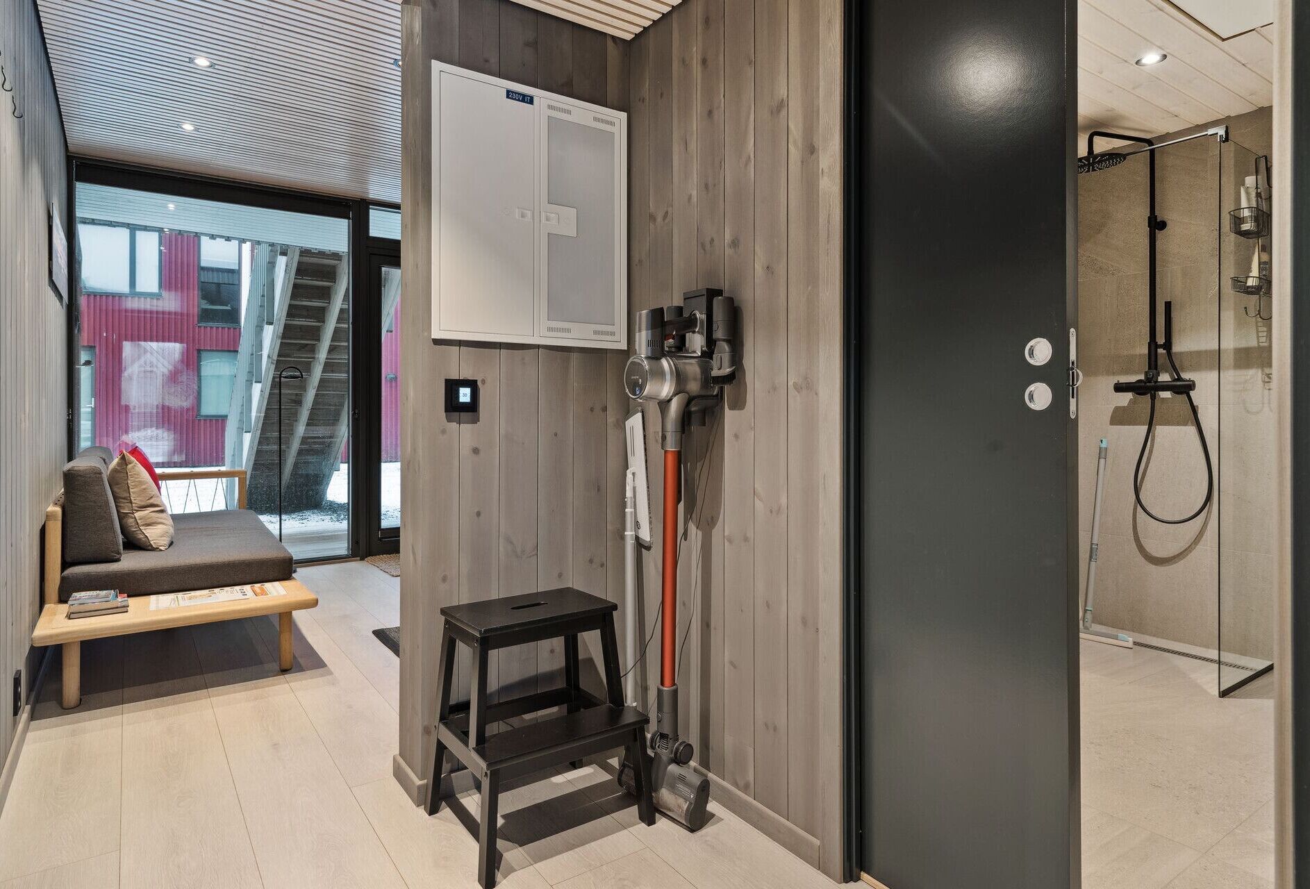 A modern bathroom with a shower, a bench, and a vacuum cleaner.