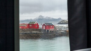 A window view of red buildings by the water, a bed, and a curtain.
