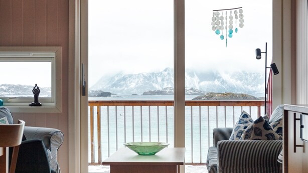 A living room with a view of a snowy mountain and ocean, a green bowl on a table, and striped furniture.
