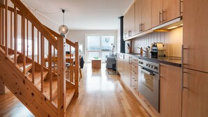 A modern kitchen with wooden cabinets, a built-in oven, and a staircase leading to a living area.