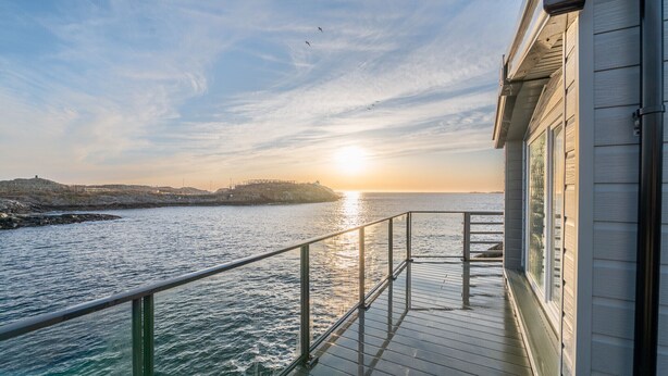A deck with a railing overlooking a body of water, a distant shoreline, and a clear sky.