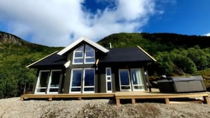 A modern house with a large front porch, multiple windows, and a view of a forested hillside.