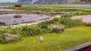 A coastal landscape with mountains, a grassy area, and a red railing.