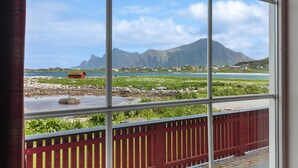 A view through a window with a red railing, a body of water, and distant mountains.