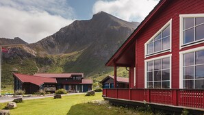A red building with large windows, a stone foundation, and a mountain backdrop.