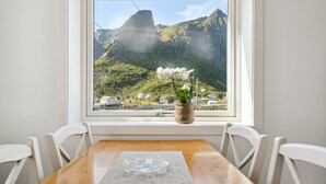 A dining table with chairs, a window with a view of mountains, and a potted plant on the windowsill.
