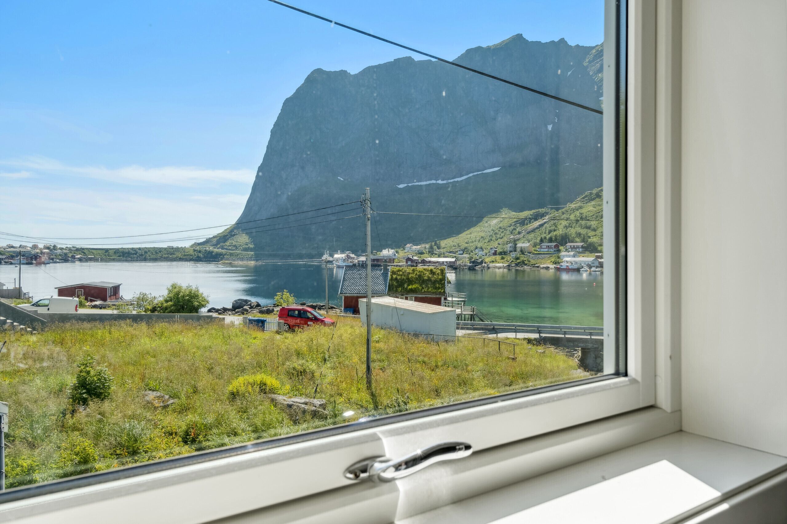 A window view of a coastal area with a mountain, water, and buildings.