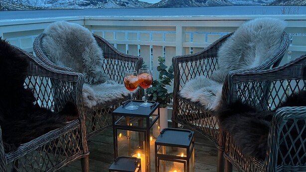 A cozy outdoor seating area with wicker chairs and a table, candles, and a view of snow-capped mountains.