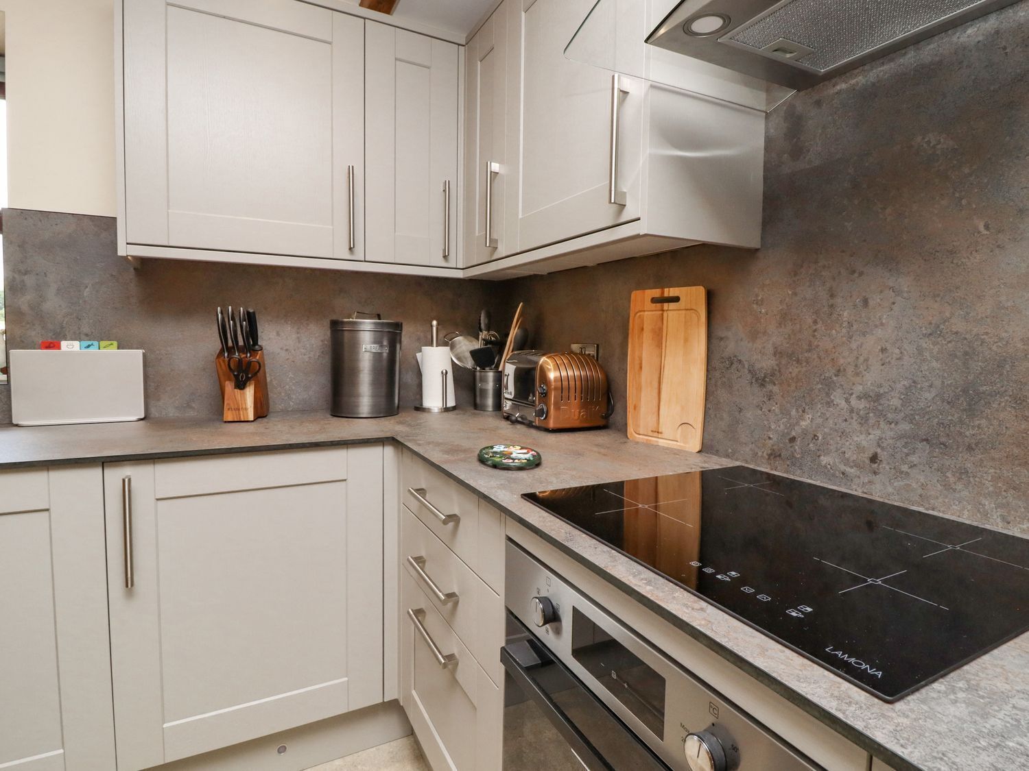 A modern kitchen with white cabinets, a black induction cooktop, and a built-in oven.