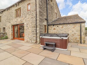 A stone building with a large sliding glass door, a hot tub, and a tiled patio. - Orcaber Farmhouse (Lancaster)