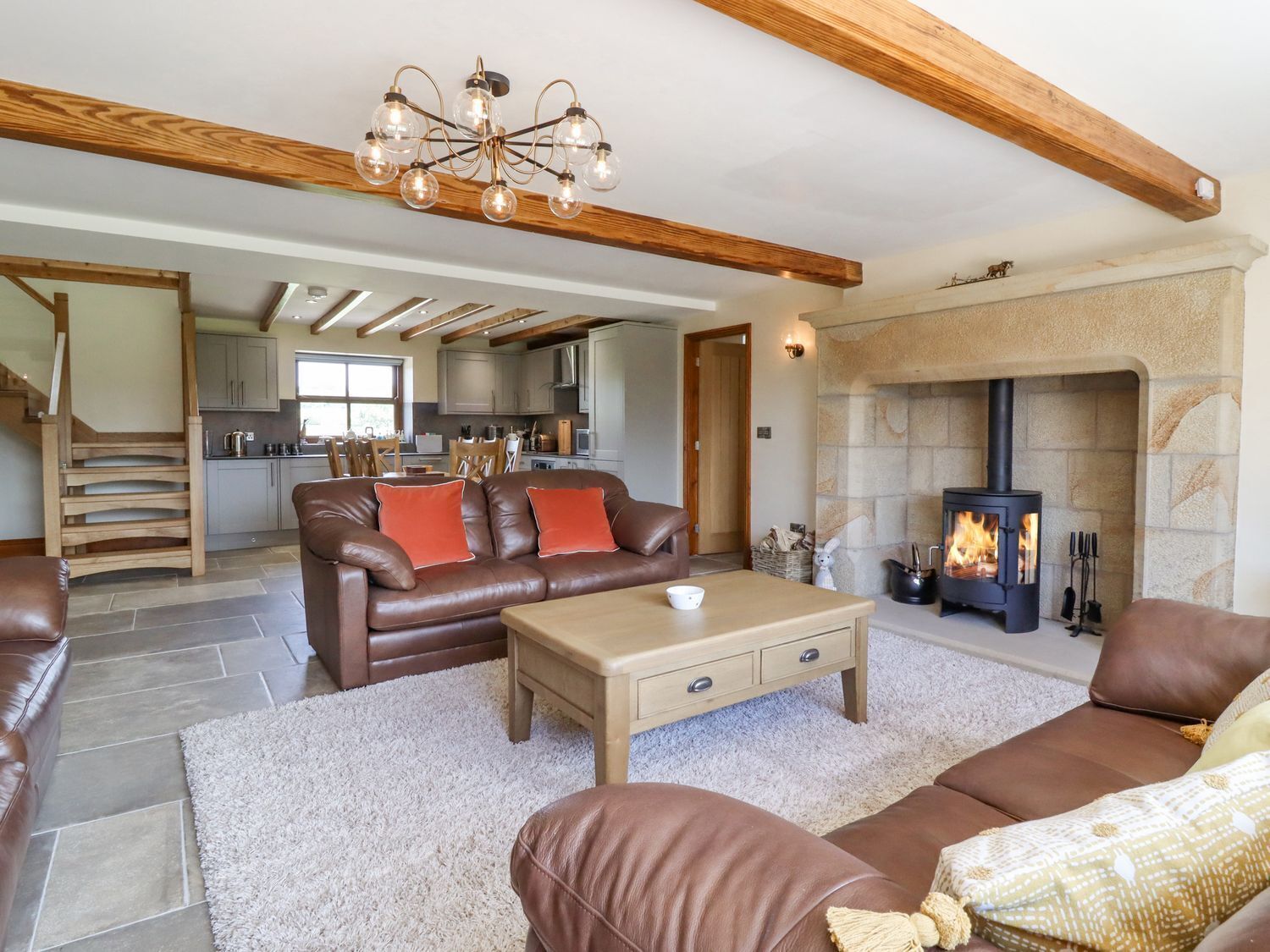 A spacious living area with a fireplace, a sofa set, a coffee table, and a kitchen in the background.
