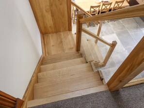 Una escalera de madera con barandilla, escalones alfombrados y un área de comedor al fondo.